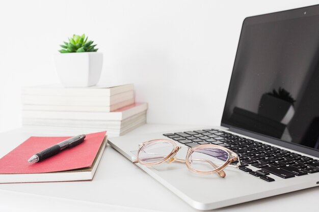 Close-up of laptop; spectacles; pen and diary on desk