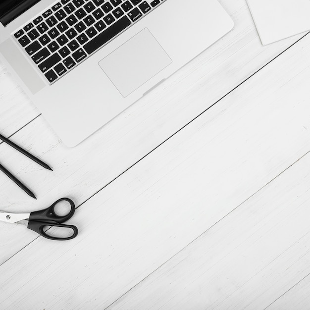 Close-up of laptop with black felt tip pen and scissor on wooden desk