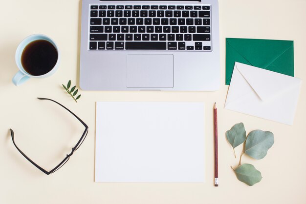 Close-up of laptop with envelope; paper; pencil; eyeglasses; tea cup and eyeglasses on colored backdrop