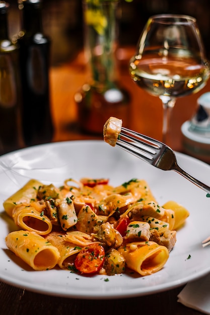Close up of large tube pasta with chicken and cherry tomato with chopped parsley