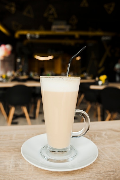 Close-up of latte coffee cup with straw and saucer on wooden desk