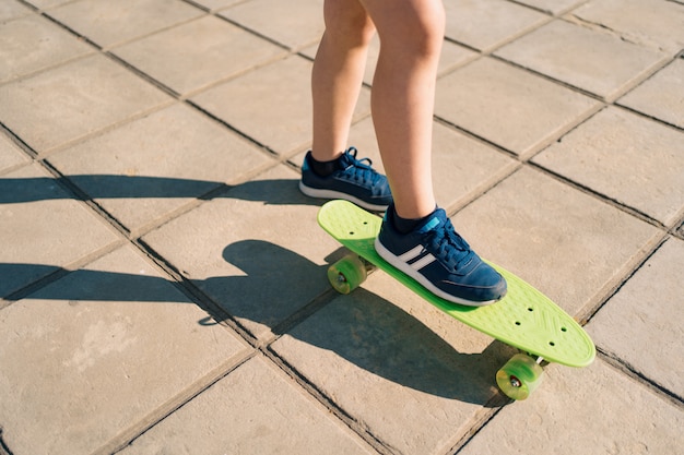 Close up legs in blue sneakers riding on green skateboard in motion. Active urban lifestyle of youth, training, hobby, activity. Active outdoor sport for kids. Child skateboarding.