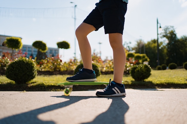 Close up legs in blue sneakers riding on green skateboard in motion. Active urban lifestyle of youth, training, hobby, activity. Active outdoor sport for kids. Child skateboarding.