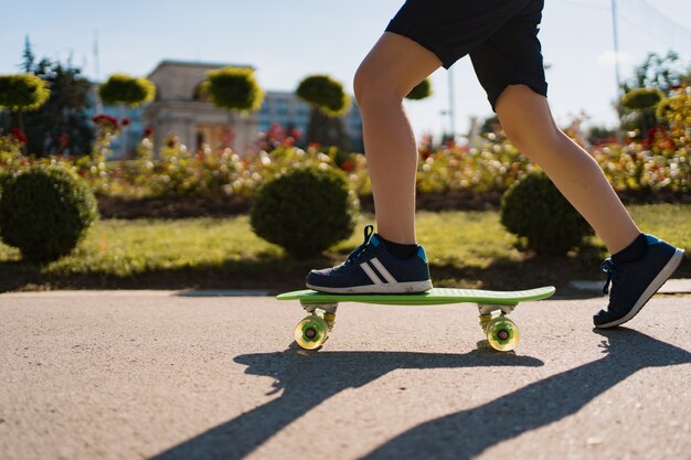 Close up legs in blue sneakers riding on green skateboard in motion. Active urban lifestyle of youth, training, hobby, activity. Active outdoor sport for kids. Child skateboarding.