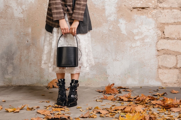 Close up legs in boots of stylish woman in jacket walking against wall in street