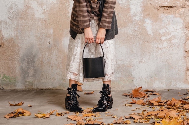 Close up legs in boots of stylish woman in jacket walking against wall in street