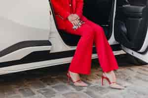 Foto gratuita chiudere le gambe con i tacchi e le mani che tengono i bicchieri di bella donna d'affari ricca sexy in vestito rosso che posa in macchina bianca