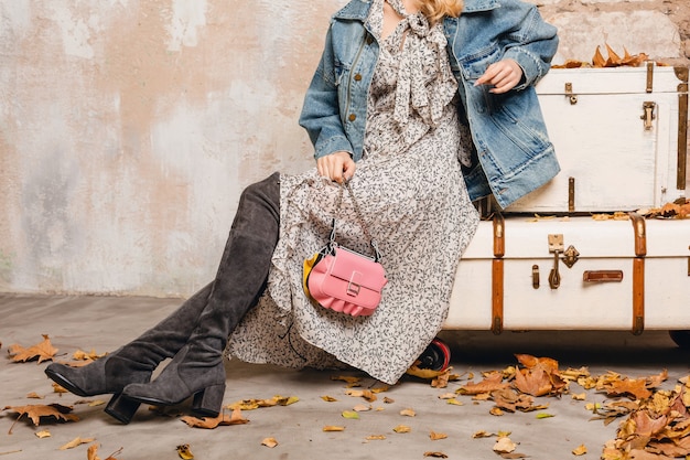 Chiudere le gambe in stivali alti in pelle scamosciata di donna alla moda in jeans e giacca oversize contro il muro in strada