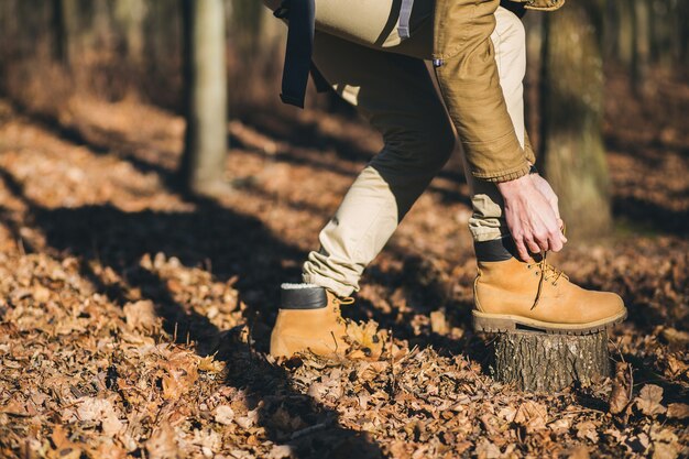 가을 숲을 여행하는 힙스터 남자의 신발을 추적하는 다리를 닫습니다