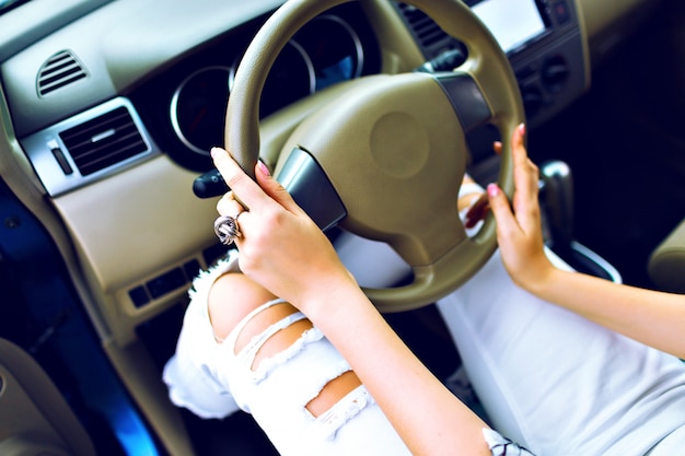 Close up lifestyle image of stylish woman driving her car, perfect manicure and accessory, vintage denim crazy pants, travel road concept.