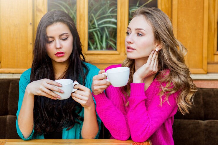 Free Photo close up lifestyle portrait of  two beautiful  young   friends sitting in cafe and enjoying  hot tee . wearing bright neon yellow , and pink  stylish  sweater .holidays, food and tourism concept .