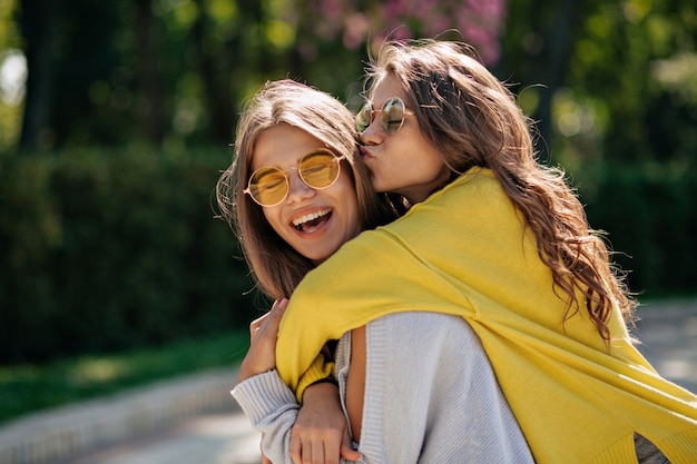 Close up lifestyle portrait of two happy inspired teen friends hugs and smiling. Best female friends having fun and walking in the sunny summer park. Wearing casual outfit .