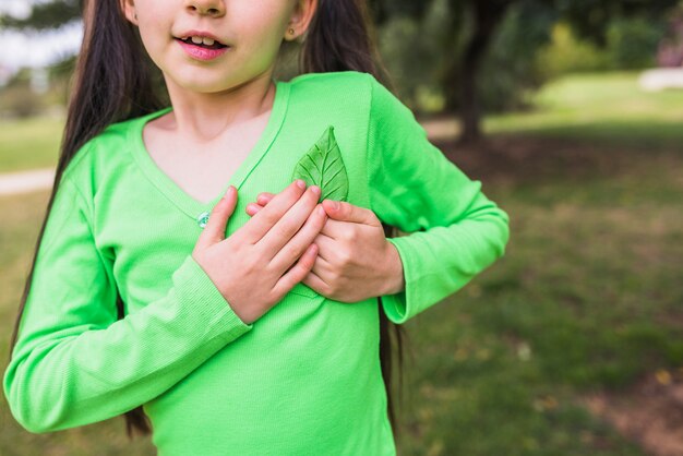 Close-up of a little girl holding fake green leaf near heart