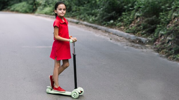 Крупный план маленькая девочка, стоящая на нажимном скутере