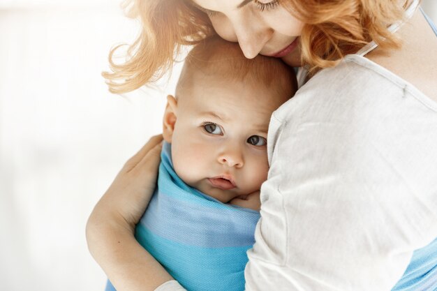 Крупным планом маленький ребенок с большими серыми глазами, глядя в сторону в прекрасных руках матери