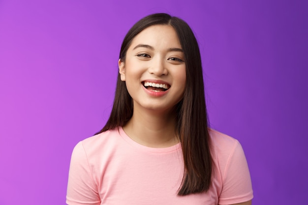 Close-up lively carefree cheerful asian girl laughing, having fun, smiling amused enjoy friendly relaxing conversation, stand purple backgrond joyful, look camera upbeat. Copy space