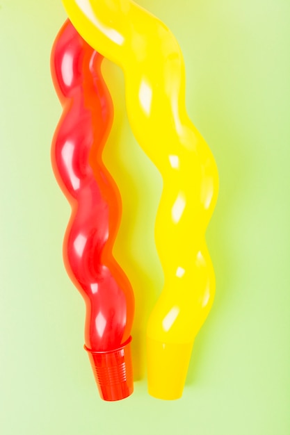 Close-up of long red and yellow balloon over the plastic cup against the green background