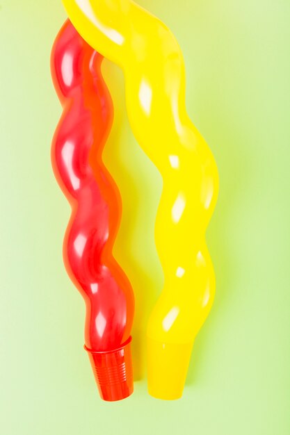 Close-up of long red and yellow balloon over the plastic cup against the green background