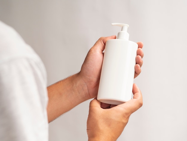 Free photo close-up lotion bottle mock-up holding by hands