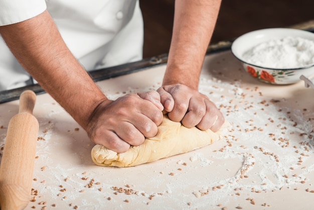 Крупный план сделать пекарский рука, замешивая тесто на кухонном столе
