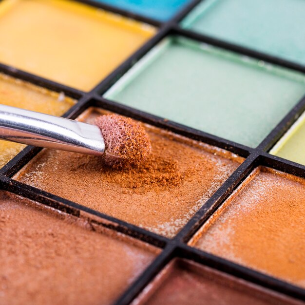 Close-up of makeup brush with palette of colorful eye shadows