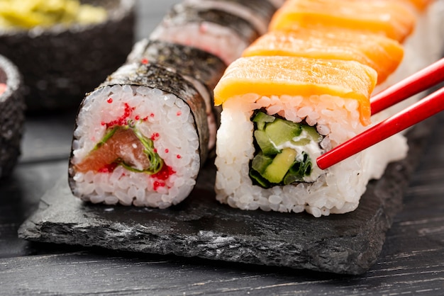 Foto gratuita sushi di maki del primo piano sull'ardesia con le bacchette