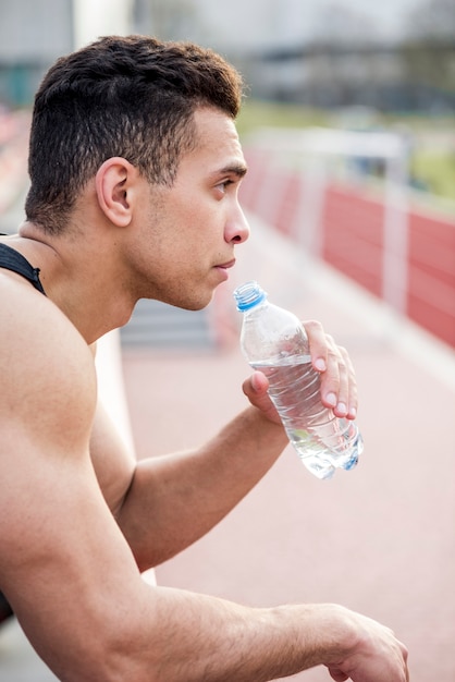 Foto gratuita primo piano di un distogliere lo sguardo disponibile della bottiglia di acqua maschio della tenuta dell'atleta