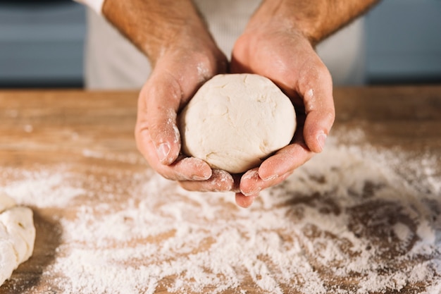 Close-up of male baker holding knead dough in hand over the wooden table