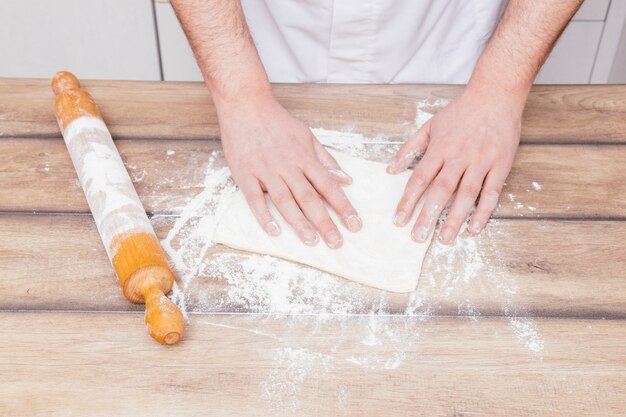 Крупным планом мужской пекарь готовит тесто на деревянный стол