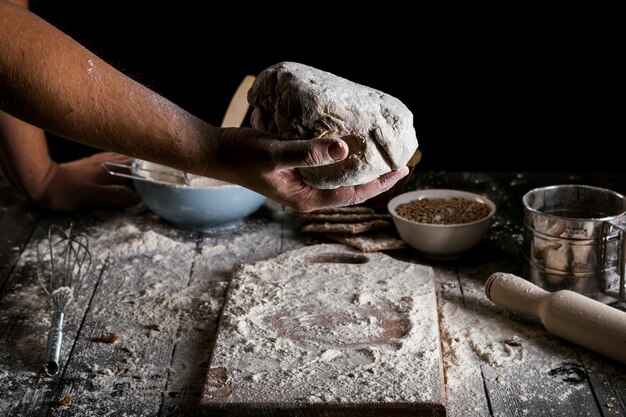 Крупный план мужского пекаря рука, замешивая тесто