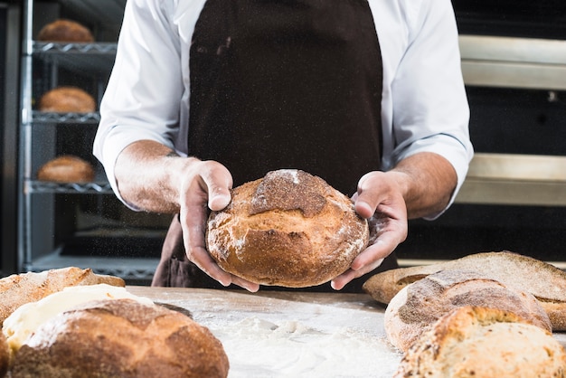 Крупным планом мужской пекарь, показывая буханку хлеба