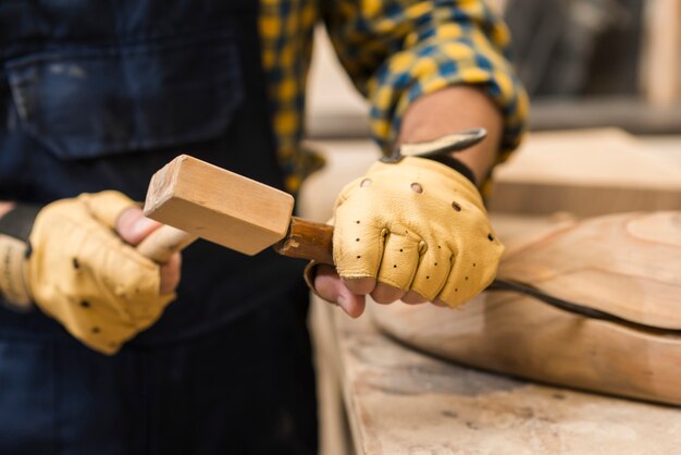 Close-up of a male carpenter hitting chisel on wooden structure with hammer