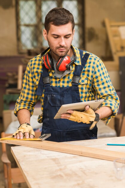 Close-up of a male carpenter looking at digital tablet measuring the wooden block