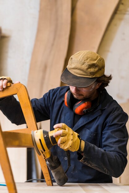 Close-up of a male carpenter sanding furniture with power tool on workbench