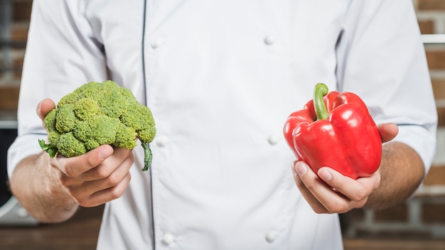 Close-up of male chef holding fresh red bell pepper and broccoli