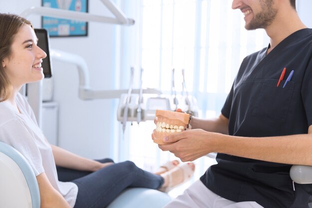 Крупный план стоматолога-мужчины, демонстрирующего модель зубов пациенту