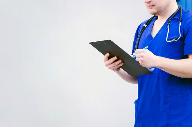 Close-up of a male doctor examining the clipboard with pen isolated against grey background