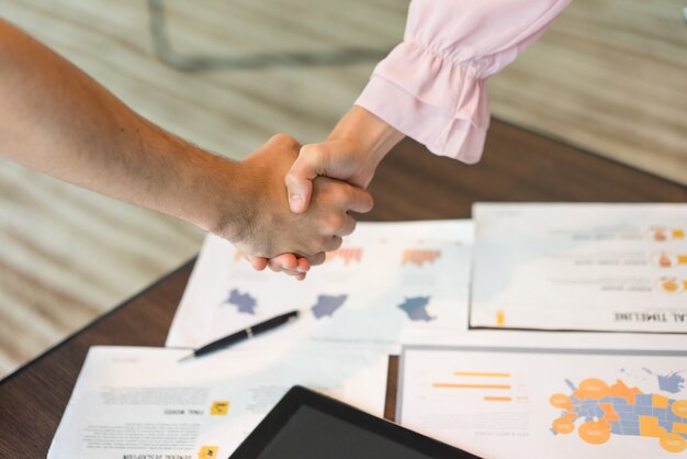 Close-up of male and female hands in handshake over documents.