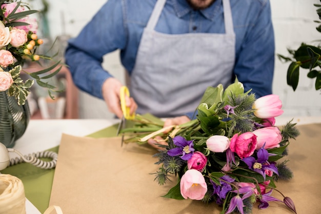 花の花束を包むための紙を切る男性の花屋のクローズアップ