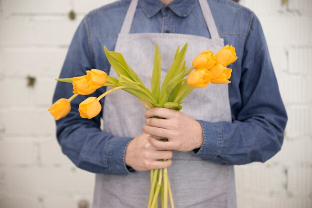 Крупным планом мужской флорист держит желтые тюльпаны на белой стене