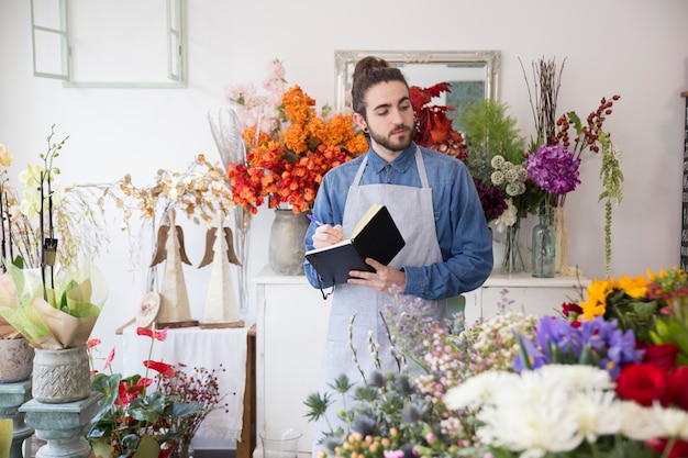 Close-up of a male florist looking at flower bouquet writing in the diary with pen