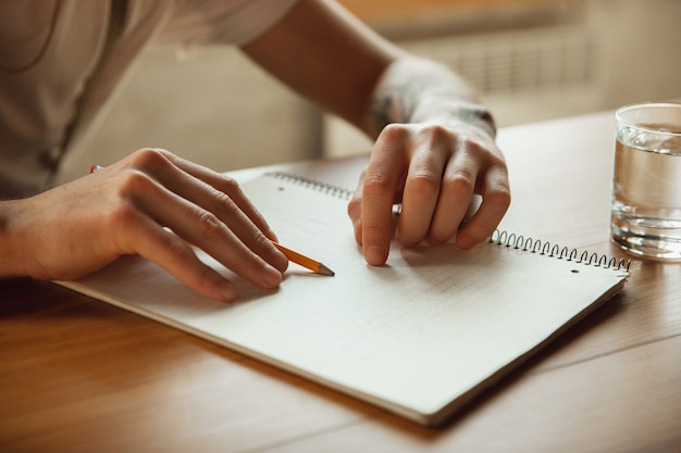 Close up of male hands writing on an empty paper on the table at home. Making notes, workhome, report for his work. Education, freelance, art and business concept. Leaves signature, doing paperwork.