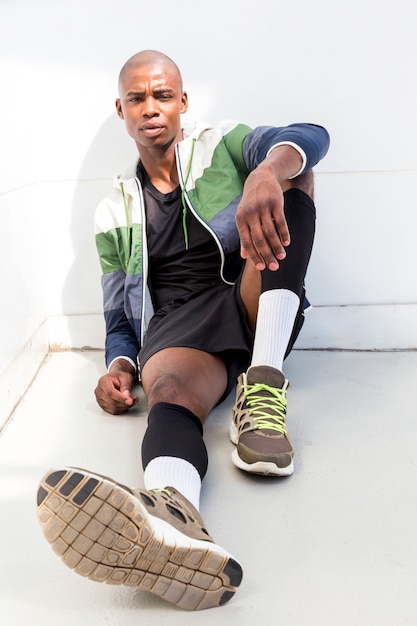 Close-up of a male runner relaxing against white wall looking at camera