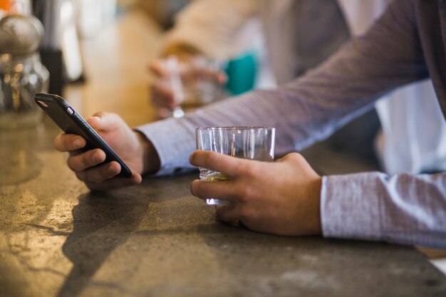 Крупным планом рука мужчины, проведение стакан напитков с помощью мобильного телефона