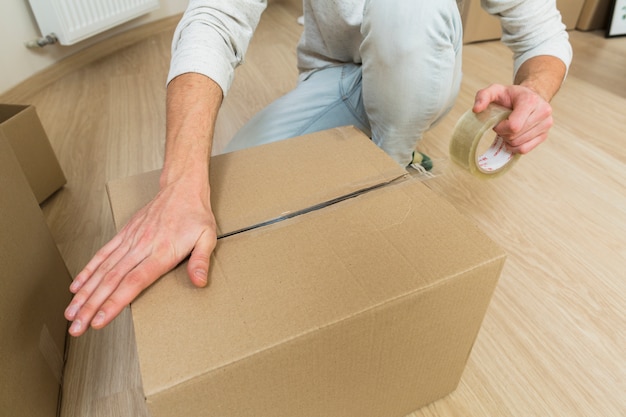 Close-up of male sealing cardboard box with adhesive tape