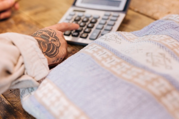 Free photo close-up of male seller using calculator near the textile fabric on wooden table in shop