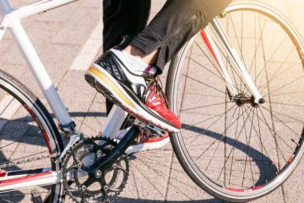 Close-up of male wearing jeans and wearing sport shoes rides bicycle on the park
