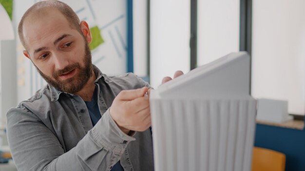 Close up of man analyzing building model with woman using blueprints plan on table. Colleagues working together to design construction structure and layout for urban development.