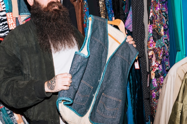 Primo piano di un uomo in un negozio di abbigliamento che tiene in mano giacca di pelliccia di jeans