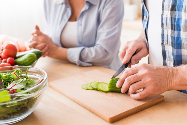 Close-up of man cutting the cucumber with knife on chopping board